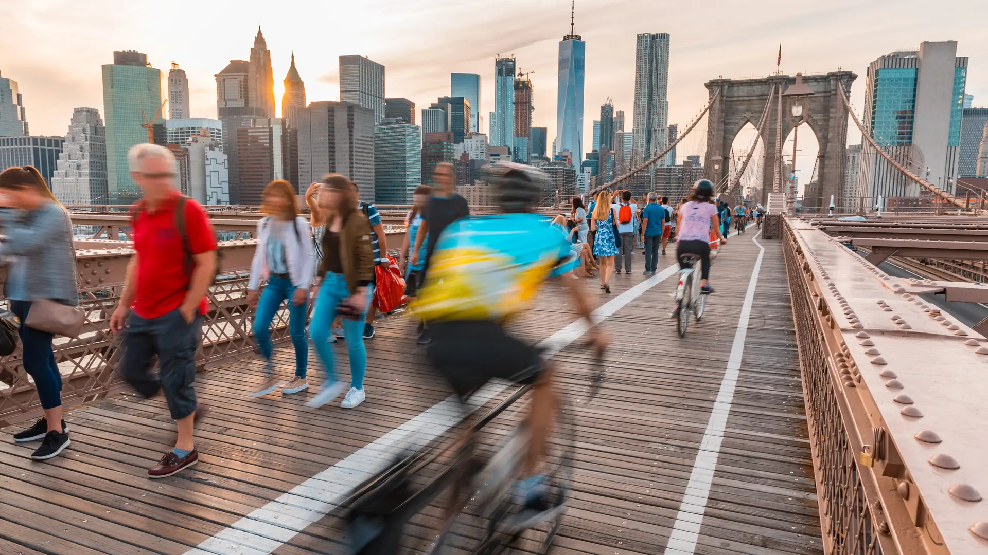 Cyclists crossing the Brooklyn Bridge toward the Manhattan skyline at sunset